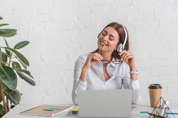 Wall Mural - happy businesswoman listening music in headphones while relaxing in office