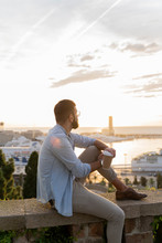 Man Sitting On A Wall On Lookout Above The City With View To The Port, Barcelona, Spain