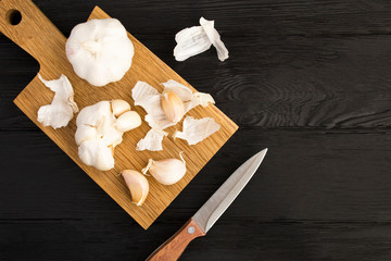 Wall Mural - Dry garlic on the brown cutting board on the black wooden background. Top view. Copy space.