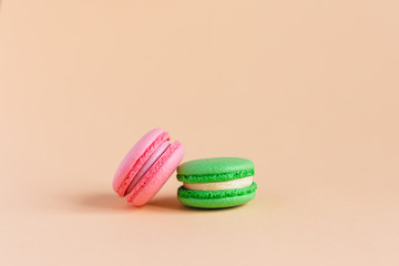 Two tasty french macarons on peach pastel background.  Pink and green macarons. Close-up. Place for text.