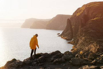 Wall Mural - Tourist in yellow jacket looks at cliffs near Sorvagsvatn lake on Vagar island, Faroe Islands, Denmark. Landscape photography