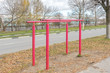 © Andrey - Iron parallel bars with peeling red paint for pulling up are installed next to roadway. Sports equipment. Autumn landscape