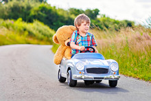 Little Preschool Kid Boy Driving Big Toy Car And Having Fun With Playing With His Plush Toy Bear, Outdoors. Child Enjoying Warm Summer Day In Nature Landscape.