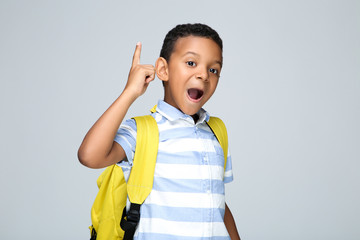 Young African American school boy with backpack on grey background