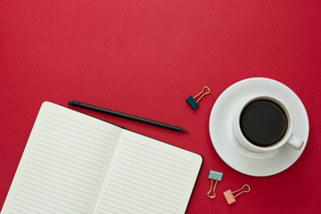 Table top, working desk with open notebook and coffee cup on red background. Copy space for text.