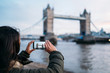 Woman taking a photo with the smart phone to the Tower Bridge in London on a sunny winter day, London, Great Britain.