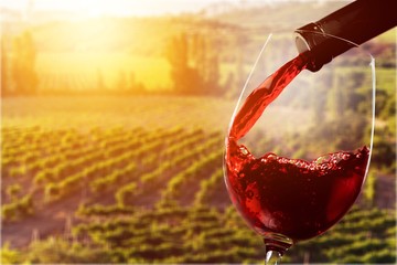 Wall Mural - Red wine being poured in wineglass on background