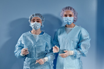 Two women doctors surgeons standing and looking at the camera on blue bakcground