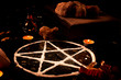 Pentagram made of salt, a pagan symbol used for protection by the wiccan community,  surrounded by candles, herbs and spices on a black shiny table top.