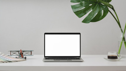 Close up of workspace with laptop, pencils, wooden figure, dry roses vase and cup on white desk with white wall