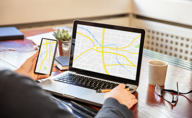 Man holding a mobile phone and working with a computer, map on the screens, office business background.