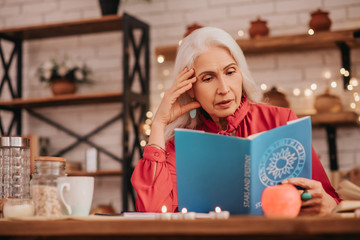 grey-haired beautiful elderly lady in red blouse reading a book