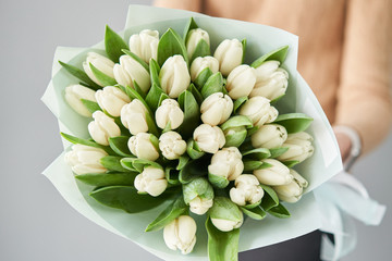 Young beautiful woman holding a spring bouquet of yellow tulips in her hand. Bunch of fresh cut spring flowers in female hands