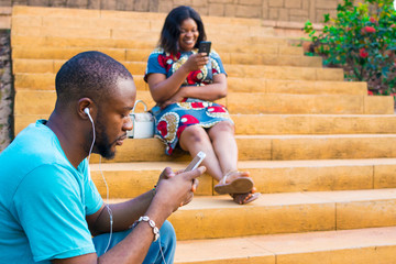 young black man and woman sitting on a staircase outside using their smartphones