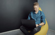 © MYDAYcontent - Smiling guy working on laptop holding it on his lap while sitting on yellow bean bag chair