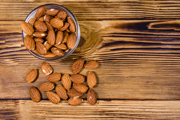 Glass bowl with the peeled almond nuts on wooden table. Top view