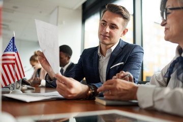 Wall Mural - Young businessman sitting and reading document to the senior businesswoman during press conference