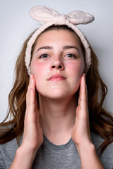 Wall Mural - Portrait of woman applying cream on a clean fresh face on gray background.