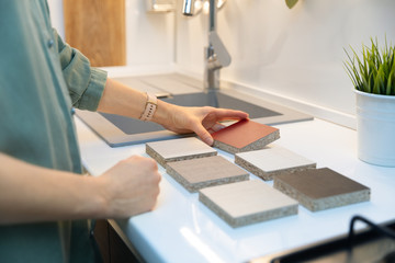 Wall Mural - woman choosing kitchen countertop material texture from samples