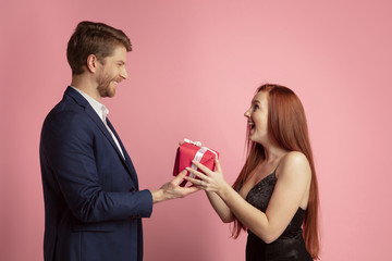 Wall Mural - giving a gift. valentine's day celebration, happy caucasian couple isolated on coral studio backgrou