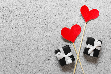 Valentine day celebration greeting card with two red hearts on wooden sticks and two little presents with white bows on stone texture background.