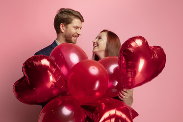 Wall Mural - happy holding balloons shaped hearts. valentine's day celebration, happy caucasian couple on coral b