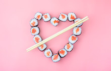 Salmon Sushi Rolls Laid Out In The Shape Of A Heart On A Pink Background. The Concept Of Japanese Cuisine For Valentine's Day, Greeting Card, Banner. Copy Space