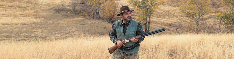 Wall Mural - Hunting period, autumn season open. A hunter with a gun in his hands in hunting clothes in the autumn forest in search of a trophy. A man stands with weapons and hunting dogs tracking down the game..