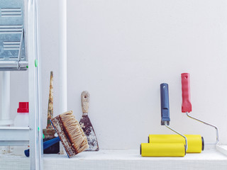 Internal repair of the room. Preparation for paint work. Various brushes, rollers and scraper are near the white wall.