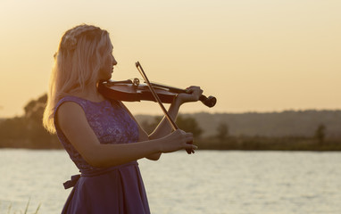 Wall Mural - romantic silhouette of young woman with a violin at dawn on river bank, elegant girl playing a musical instrument on nature, concept music and inspiration