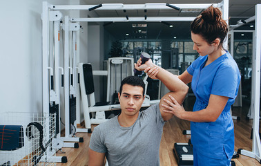 Mixed races athlete with a shoulder injury in a rehabilitation center. Physiotherapist helps recover after an injury