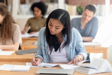 Focused Asian girl study in library writing in textbook