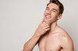 © LIGHTFIELD STUDIOS - smiling sexy man with muscular torso touching chin isolated on grey