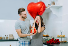 Attractive Young Couple Dressed In Casual Outfit Celebrating St. Valentine's Day Together At Home Sharing Presents In Cozy Kitchen