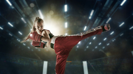 Extreme. Young female kickboxing fighter training in the gym. Caucasian blonde girl in red sportswear practicing in martial arts. Concept of sport, healthy lifestyle, motion, action, youth.