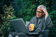 © bnenin - Stressed mature woman looking at laptop in the garden, portrait.