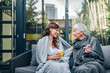 Two women of different age sitting on the patio covered in blankets and talking, portrait.