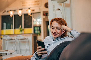 Smiling woman using smart phone indoors, portrait.