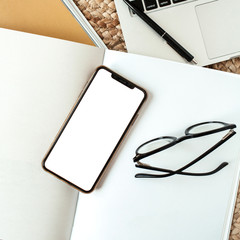 Wall Mural - Blank screen mobile smart phone with empty copy space, laptop, glasses. Flat lay, top view home office desk table workspace. Girl boss business template for social media, blog, magazine.