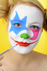 woman is making up her face as a clown for carnival or halloween