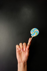 Wall Mural - Lollipop in hand on a black background, empty place for text