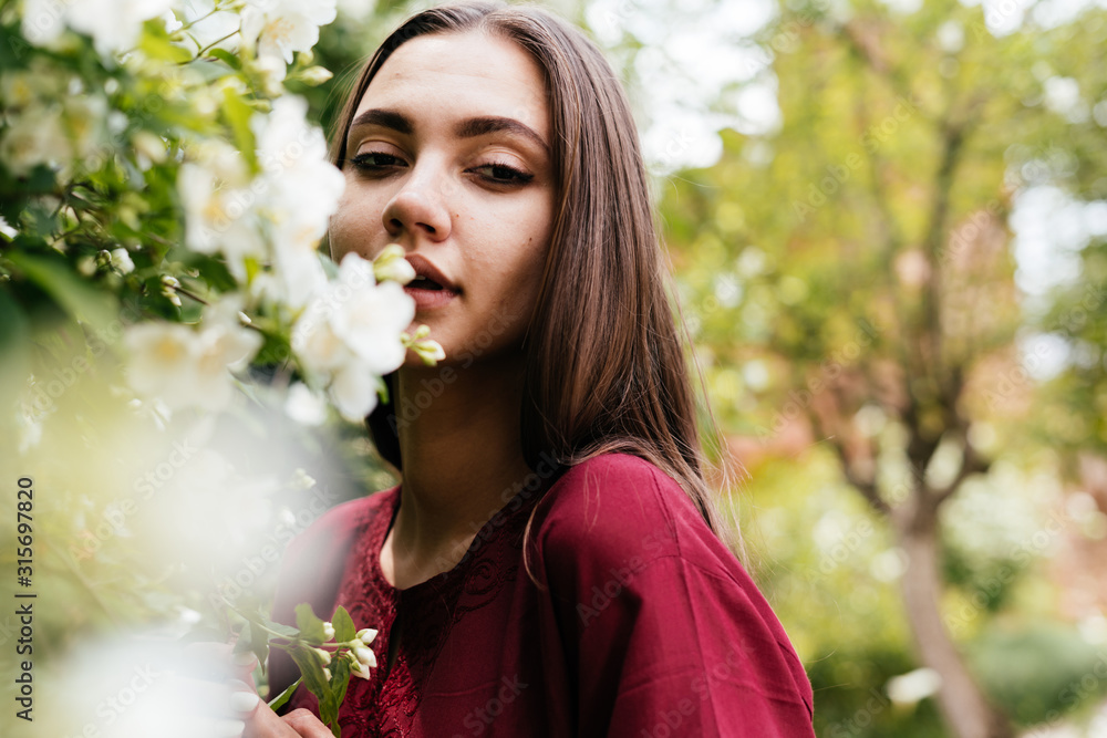 portrait of a girl gently touching her lips to a flowering jasmine bush ...