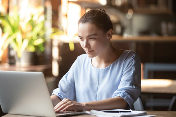 Focused young woman busy typing on laptop studying