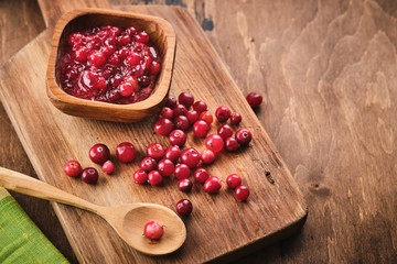 Cranberry jam in a wooden bowl on a wooden background.