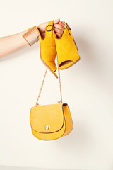 Woman hand holding yellow female fashion accessories, shoes and handbag. Beauty, shopping, urban outfit and fashion trends idea