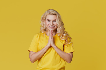 Wall Mural - Photo of a happy young blond woman standing isolated over yellow wall background. Looking at the camera showing the direction of copy space.