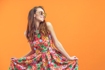 girl in floral dress emotionally poses on the orange background.