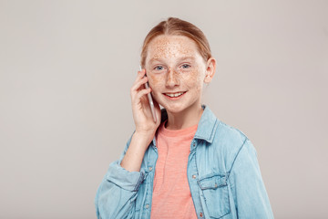 Wall Mural - Inclusive Beauty. Girl with freckles in denim jacket standing isolated on grey talking on phone smiling cheerful