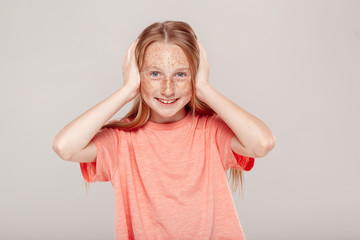 Wall Mural - Inclusive Beauty. Girl with freckles standing isolated on grey covering ears smiling cheerful