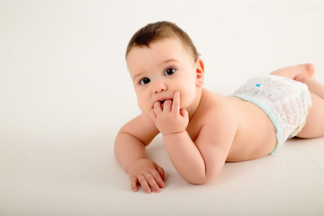 Wall Mural - healthy baby brunette boy smiling and looking at the camera, baby in a diaper lying on a white background, space for text